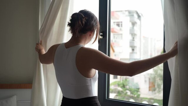Close up rear back view of silhouette young woman opens the curtains looking enjoying light and city view in the morning cloudy day Generative AI