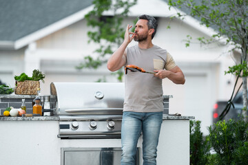 Barbecue concept. Middle aged hispanic man in t-shirt for barbecue. Roasting and grilling food. Roasting meat outdoors. Barbecue and grill. Cooking meat in backyard.