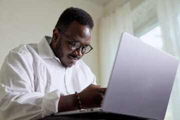 Handsome Black African American Man Working on Laptop Computer while Sitting on a Sofa in Cozy...