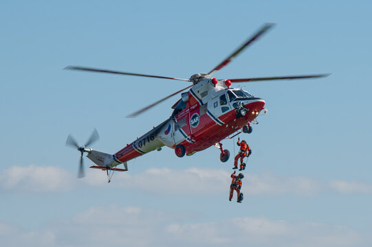 helicopter in flight with rescue unit on rope getting down to the ground