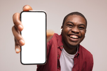 Fototapeta na wymiar Mobile advertisement. Overjoyed black man pointing at cellphone with empty white screen on blue studio background, mockup for app or website. Cellphone display template