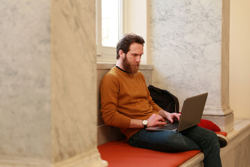 A bearded freelancer student studying with his laptop notebook in a building with natural light