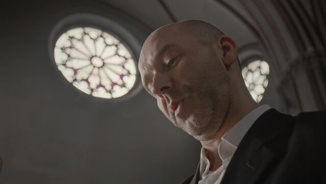 Low angle medium closeup of middle aged bald headed Caucasian pastor reading holy book in Catholic Church aloud