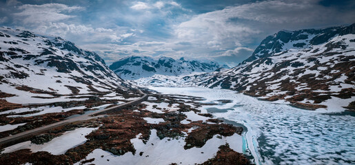 Snowy landscape of Hardangervidda national park with mountains and a road along icy lakes in Norway, from above - 598148201