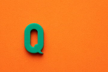 Alphabet letter Q - Green plastic piece on orange foamy background