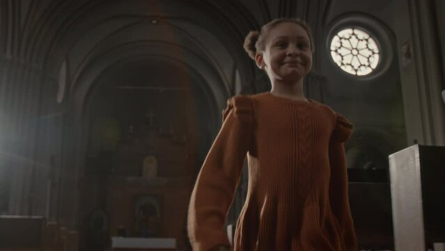 Medium slowmo of delighted African American girl running along nave in Catholic Church with sun rays shining through window