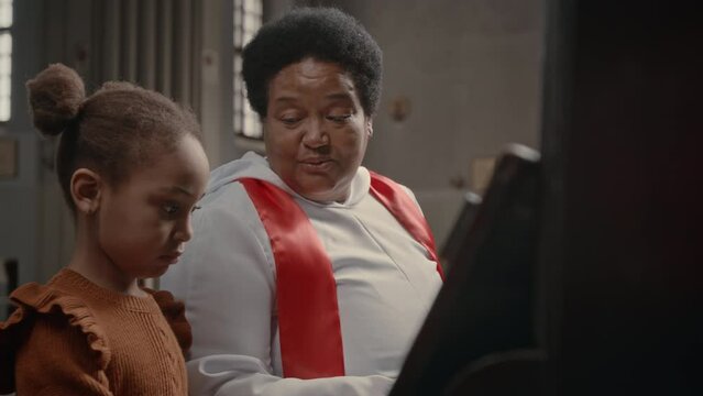 African American grandmother teaching her little granddaughter to play piano in Catholic Church