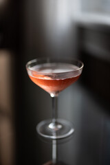 Glass of pink champagne on a glass table by a window at sunset