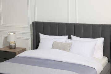 Fototapeta na wymiar Comfortable bed near lamp on bedside table in stylish bedroom