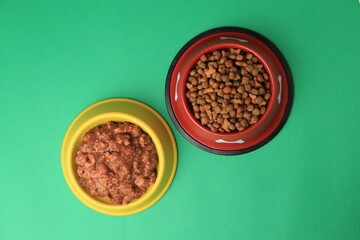 Dry and wet pet food in feeding bowls on green background, flat lay