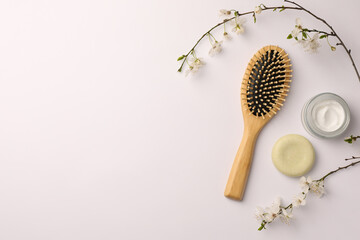 Wooden hairbrush, cosmetic products and branch with flowers on white background, flat lay. Space...