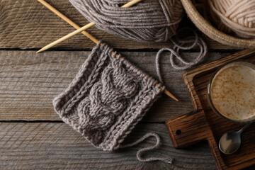 Fototapeta na wymiar Soft grey woolen yarn, knitting, needles and glass of coffee on wooden table, flat lay