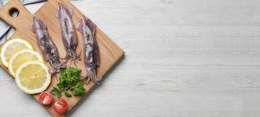 Board with fresh squids, parsley, slices of lemon and tomato on white wooden table, flat lay. Banner design with space for text