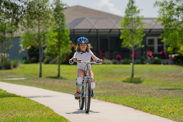 Fototapeta premium Little kid boy riding a bike in summer park. Children learning to drive a bicycle on a driveway outside. Kid riding bikes in the city wearing helmets as protective gear. Child on bicycle outdoor.