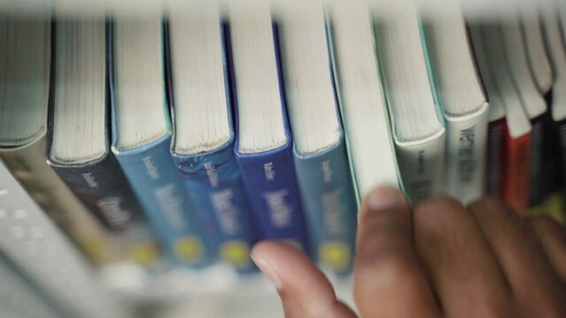 A hand moves finger along book spines until choosing on of the books. Hand held static shot