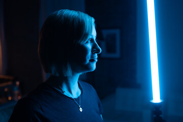 Beautiful blonde woman holding blue emitted lightsaber in a dark room.