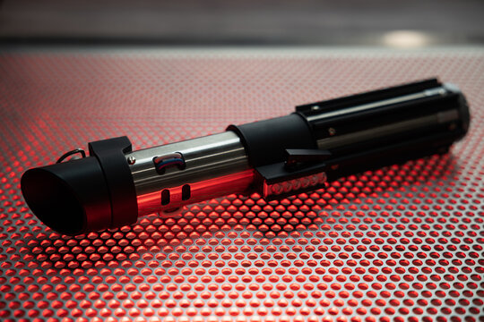 Lightsaber sitting on a table, illuminated by red light.