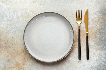 Empty beige plate, knife and fork on a brown background. Cutlery, top view.