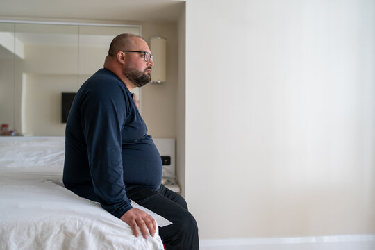 Calm Sleepy Man Waking Up In Morning At Home Sitting In Bed Ready To Start New Day, Side View. Restful Overweight Bearded Young Male In Bedroom. Early Rise, Healthy Sleeping And Generative AI