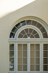 Victorian Style Arched Window with Wooden Sashes on a Wall with Sunlight and Shadow.