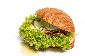 Croissant sandwich with meat, cheese and salad on a white plate, close-up, side view. Isolated on white background. Healthy breakfast concept, restaurant menu