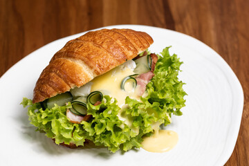 Croissant sandwich with meat, cheese and lettuce on a white plate, closeup, side view. Healthy breakfast concept, restaurant menu