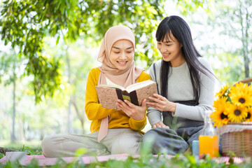 Happy beautiful Asian females Muslim student and friends reading a textbook together in a park. Diversity in ethnic and religious concept.