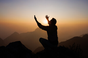 Silhouette of a man is praying to God on the mountain. Praying hands with faith in religion and...
