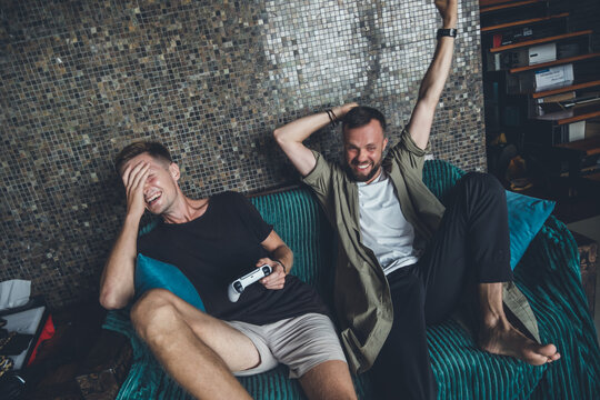 Two friends of handsome guys play a console at home, strong emotions, joy, annoyance, victory, laughter, surprise, computer games, joysticks