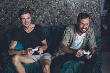 Two friends of handsome guys play a console at home, strong emotions, joy, annoyance, victory, laughter, surprise, computer games, joysticks