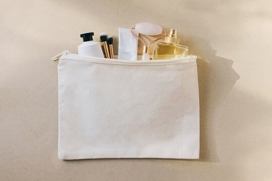 Canvas bag with cosmetics and accessories on beige background.