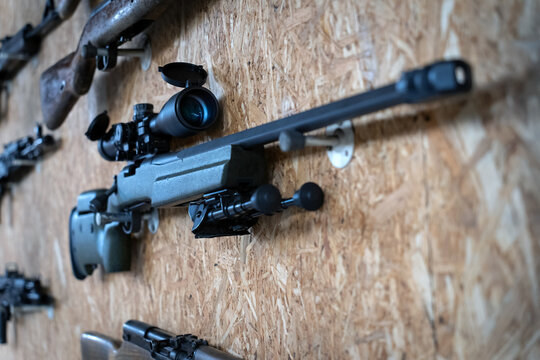 A sniper rifle with an optical sight and a bipod hangs on the wall in a shooting range.