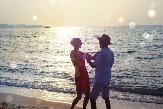 Silhouette Happy Mature couple happy retirement planning concept, Beautiful and happy senior couple in love and enjoying retirement celebrating dancing on the beach with flare and bokeh light