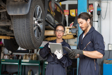 Mechanics man and woman in uniform look at digital tablet discussing car check and repair...