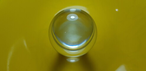 Crystal small ball on a yellow background (macro, top view, artificial lighting).
