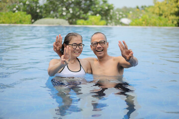 asian couple raising three finger with relaxing in swimming pool