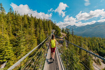 Woman hiking in mountains crossing foot suspension bridge with amazing views. Canada Tourism...