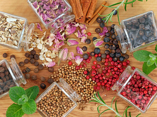 Top view of herbs and botanicals for cocktails or gin flavoring on wooden table with juniper berries, pink peppercorns, allspice, dried rose petals, sweet dried orange peels and cinnamon sticks
