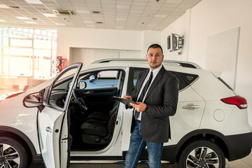 young salesman in suit standing near at car in new modern dealership