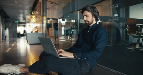 Successful Office Worker Working Comfortably on Laptop. Office worker sits on the floor near a glass wall and work on a laptop Generative AI