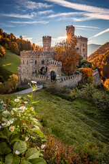 Latzfons, Italy - Beautiful autumn scenery at Gernstein Castle (Castello di Gernstein, Schloss Gernstein) at sunrise in South Tyrol with blue sky and golden foliage and flowers at foreground