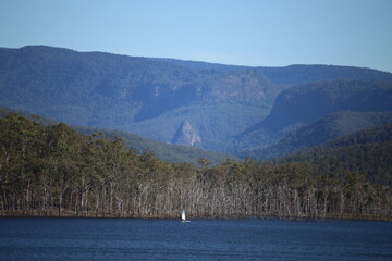 Sailing Boat on Blue Lake with Mountains and Green Trees in the background