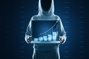 Hacker in hoodie holding laptop with growing blue financial coins chart on blurry background....