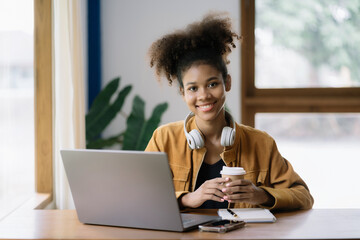 Happy black businesswoman using a smartphone and laptop in a creative home office.