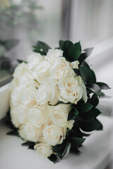 A bouquet of white roses and greenery on a white background. A beautiful photo with details of the wedding. Wedding day. Daylight.