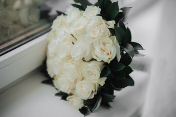 A bouquet of white roses and greenery on a white background. A beautiful photo with details of the wedding. Wedding day. Daylight.
