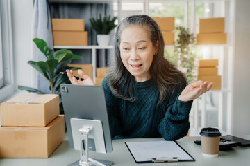 Startup small business entrepreneur or freelance older woman using a laptop with box, checking orders from customers, online marketing delivery, SME