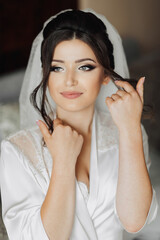 Portrait of a brunette bride touching her face. Gorgeous make-up and hair. Voluminous veil. Wedding photo. Beautiful bride