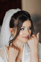 Portrait of a brunette bride touching her face. Gorgeous make-up and hair. Voluminous veil. Wedding photo. Beautiful bride