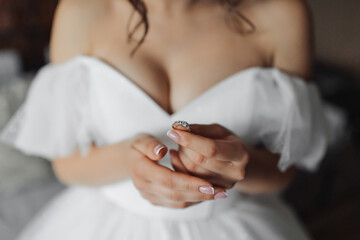 A brunette bride in a white dress holds her silver wedding ring. French manicure. Open shoulders....